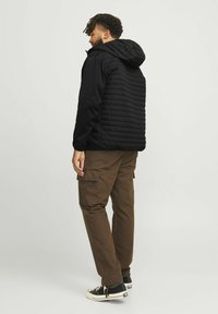 Sort polstret jakke med hætte, med en struktureret, quiltet bagpanel. Sammen med brune cargo bukser og sorte sneakers.