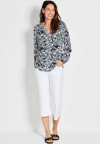 Blusa a maniche lunghe con motivo a foglie blu e nere, con bottoni sul davanti, abbinata a pantaloni bianchi a trama corta e sandali neri a scivolo.