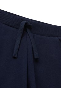 Tmavě modré tepláky s páskem z ribované gumy a rozvázaným tkaným stahovacím šňůrkou visícími vpředu.