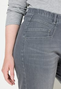 Jeans de mezclilla gris con un diseño ajustado, que cuentan con dos bolsillos traseros y un tejido suave, ligeramente texturizado. Cintura elástica para mayor comodidad.