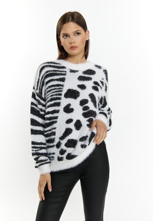 Un pull flou noir et blanc avec un mélange de rayures de zèbre et de taches de léopard, à ourlet arrondi et coupe décontractée, associé à un pantalon noir.
