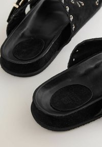 Sorte ruskindssandaler med et åbent design, der har snører detaljer og en struktureret sort gummisål. Indersålerne er glatte og afrundede.