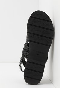 Schwarze geflochtene Sandalen mit strukturiertem, gewebtem Obermaterial, Gummisohle mit geprägtem Logo und Größenangabe "37" auf der Sohle.