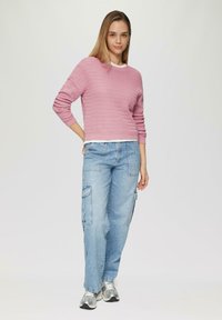 Pull en tricot texturé rose à col rond, associé à un jean cargo bleu clair avec poches latérales et des baskets argentées.