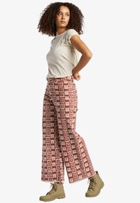 Wide-legged pants in a rust-red color with white geometric patterns, paired with a light beige t-shirt and tan boots.
