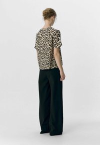 Haut léger à motif animal en beige et noir, associé à un large pantalon noir. Le haut a des manches courtes et une coupe décontractée.