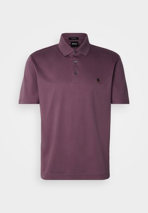 Violetti polo-paita, jossa on taitettu kaulus, kolme mustaa nappia ja pyöreä logodetail vasemmassa rinnassa. Lyhyet hihat ja sileä kangas.