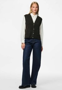 Tmavě šedý vlnený svetr s výstřihem do V, se dvěma předními kapsami a čtyřmi knoflíky, přeložený přes bílou košilovou košili a doplněný o tmavé modré široké džíny.