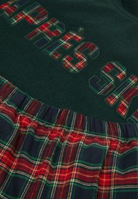 Sweatshirt vert avec de grandes lettres en tartan ; jupe à carreaux assortie avec un motif à carreaux rouge, vert, jaune et bleu ; taille élastique.