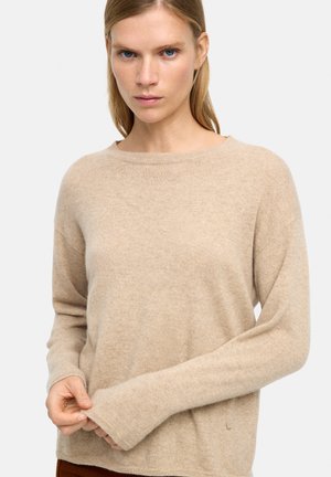 Beżowy sweter kaszmirowy o luźnym kroju, okrągłym dekolcie, długich rękawach i ściągaczach. Miękka tekstura z minimalnym logo na krawędzi.