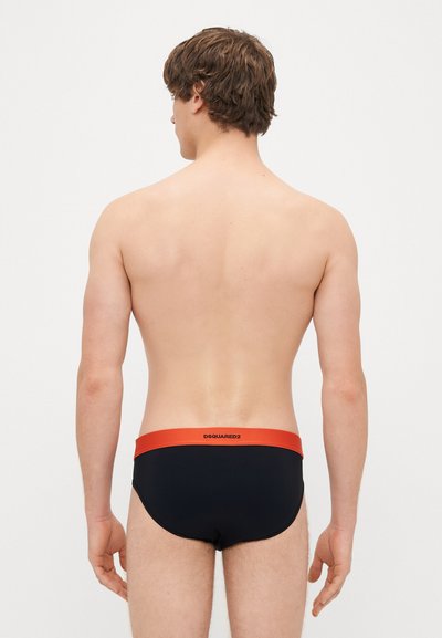 Μαύρα μαγιό με λεπτή σχεδίαση που διαθέτουν ζώνη σε αντίθεση πορτοκαλί χρώματος με το όνομα της μάρκας. Λείο υλικό και εφαρμοστό σχέδιο με μέτρια κάλυψη.