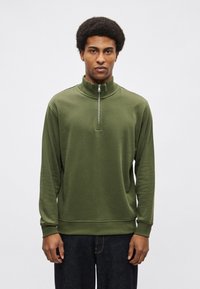 Õlirikkast rohelise tooniga veerandlukuga pusa pehmest kangast. Omadusteks kõrge krae ja soonikkoes mansetid, lõdvestunud lõige ning külgpaneli detailid.