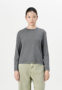 Grey long-sleeve top with a round neckline and relaxed fit. Fabric appears soft with visible stitching. Paired with light green trousers.