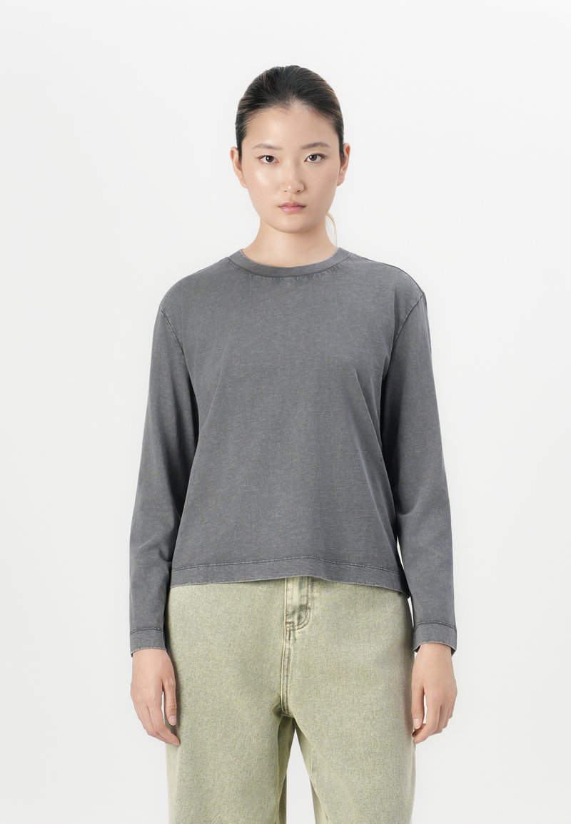 Grey long-sleeve top with a round neckline and relaxed fit. Fabric appears soft with visible stitching. Paired with light green trousers.