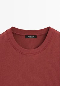 T-shirt en coton couleur rouille à col rond, avec des coutures visibles et une étiquette noire à l'intérieur du col portant la mention « Massimo Dutti ».