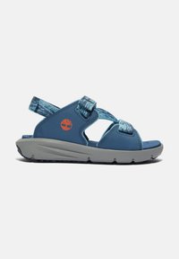 Sininen sandaali, jossa on teksturoidut nauhadesign, säädettävät Velcro-suljinnaukset ja harmaa kumipohja, jossa on oranssi logo.