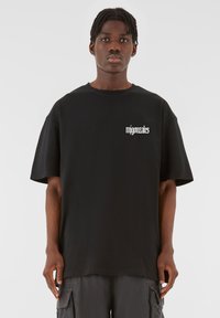 Sort oversized t-shirt med et hvidt "migonzales" logo på venstre bryst. Lavet af glat stof, med rund halsudskæring og korte ærmer.