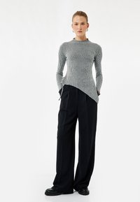 Grijze geribbelde longsleeve top met een asymmetrische zoom. Gepaarde met wijde zwarte pantalons en stevige zwarte schoenen. Minimalistisch ontwerp.