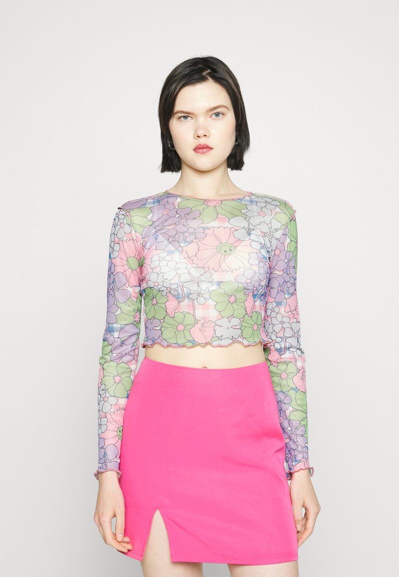 Top cropped de mangas longas em tecido transparente com flores em tons de rosa pálido, verde e roxo; combinado com uma saia mini rosa brilhante com uma fenda lateral.
