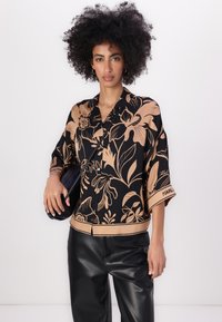 Sort skjorte med blomsterprint og tan design har krave, kortærmede ærmer og et mærket kant. Matcher med sorte faux læderbukser.