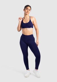Navy niebieski zestaw sportowy: biustonosz z cienkimi ramiączkami oraz wysokie legginsy, wykonane z gładkiego materiału o dopasowanym kroju. Zawiera detale z logo.