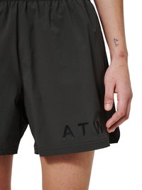 Nærbillede af en person iført sorte shorts med elastisk talje og blankt sort "ATW"-tekst på venstre lår.