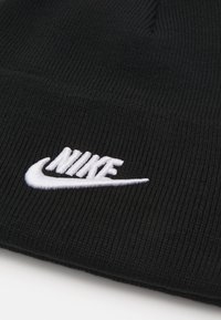 Črna pletena kapa z rebrasto teksturo. Ima bele vezenine Nike logotipa spredaj. Klasična zasnova in prilegajoč fit.