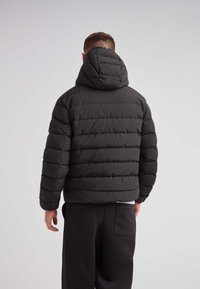 Sort pufferjakke med hætte, der har quiltede sektioner og en cropped design. Mat finish med justerbare hardware detaljer.