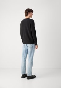 Zwart trui met ronde hals van katoen, gecombineerd met lichtblauwe recht gesneden jeans en zwarte schoenen. Eenvoudig, ontspannen pasvorm ontwerp.