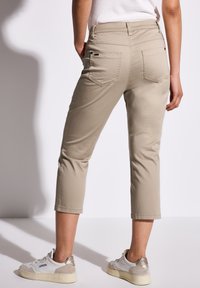 Beżowe spodnie 3/4 o gładkiej fakturze, z dwoma tylnymi kieszeniami, lekko zwężanymi nogawkami oraz subtelnymi detalami przeszyć.