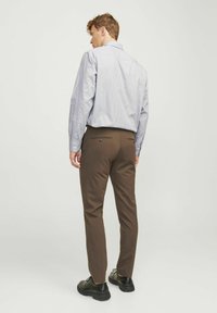 Bruine broeken en een lichtblauw gestreept shirt, beide slim fit, met een knoopsluiting op de achterzak, gecombineerd met zwarte schoenen.