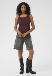 Débardeur côtelé bourgogne associé à un short en denim gris. Le modèle porte des bottes noires montantes avec des boucles et une finition lisse.