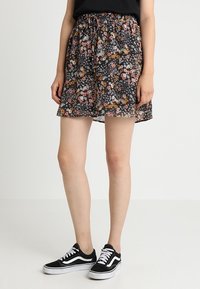 Svart blommig kjol med en färgglad tryck av små blommor, rynkad midja och ett lätt, flödande tyg. Matchas med svarta sneakers.