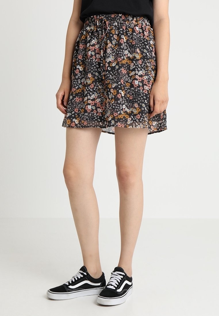 Svart blommig kjol med en färgglad tryck av små blommor, rynkad midja och ett lätt, flödande tyg. Matchas med svarta sneakers.