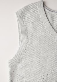 Suéter sin mangas de punto en gris claro que presenta un escote en V, un patrón texturizado y bordes acanalados, hecho de una tela suave y flexible.