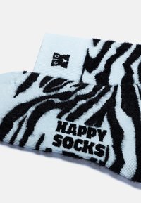 Calzini fluffosi di colore blu chiaro con un motivo a strisce zebrate nere e la scritta "HAPPY SOCKS" in lettere nere in grassetto sul polsino.