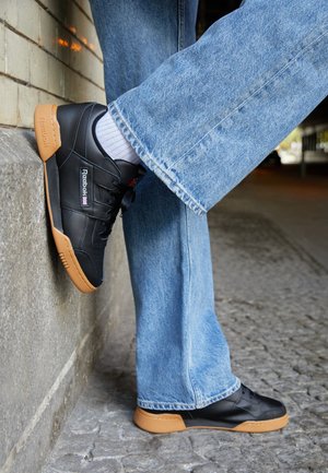 Baskets en cuir noir avec une semelle en caoutchouc gomme. Accentué d'un petit logo et d'un design à lacets. Portées avec un jean en denim clair.