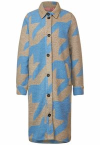 Lång, knäppt kappa i beige med djärva blå zigzag-mönster. Tillverkad av strukturerad tyg, har en krage och sidofickor.