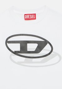 White Diesel T-shirt with red neck label and large black stylized "D" logo overlapping a gray shadow on the front.
