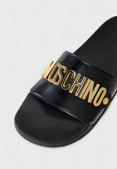 Sort slide sandal med en bred rem med præget guld "Moschino" logo. Teksturmateriale med en glat overflade. Flad såldesign.