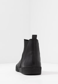 Černé kožené kotníkové boty s elastickými bočními panely, hladkým povrchem a texturovanou černou gumovou podrážkou. Mají malý podpatěk a zadní poutko pro snadné nazouvání.