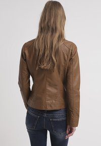 Bruine leren jas met een aansluitend ontwerp, voorzien van naaddetails en een gladde textuur, gecombineerd met denim jeans.
