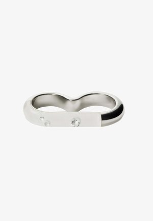 Anillo de metal plateado con una superficie lisa y pulida, que presenta tres piedras transparentes incrustadas y un acento negro en un lado.
