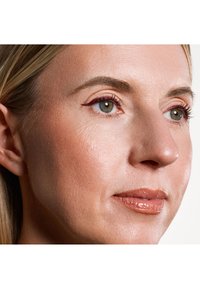 Primo piano di un volto con una texture della pelle liscia, tono beige chiaro, colore labbra sottile e trucco occhi definito con eyeliner a ala color bordeaux.