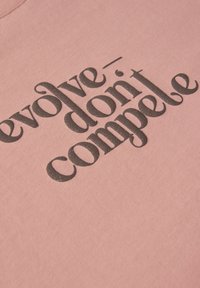 Světle růžová bavlněná mikina s černým nápisem "evolve - don't compete", s dekorativním písmem a texturovaným povrchem.