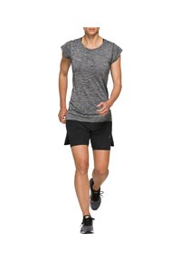 Kvinna som springer iklädd en grå kortärmad tröja, svarta shorts och svarta löparskor mot en vit bakgrund.