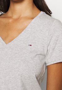 Grå bomullströja med V-ringning. Har en liten logotyp i röd, vit och blå på vänster bröst. Korta ärmar och mjuk känsla.