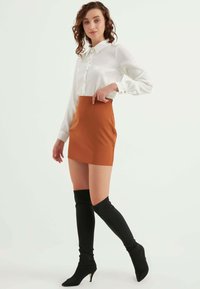 Witte blouse met lange mouwen, gecombineerd met een strakke oranje minirok en zwarte laarzen tot boven de dij. Eenvoudig ontwerp met een verzorgde uitstraling.