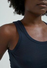 Schwarzes Baumwolltanktop mit glatter Textur, rundem Ausschnitt und breiten Trägern, das feine Nähte entlang der Kanten aufweist.