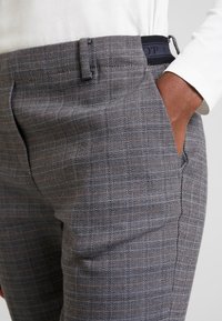 Grå rutiga byxor med subtila orange accenter. Har platt front, sidofickor och en texturerad tyg. Detaljerad elastisk midja.